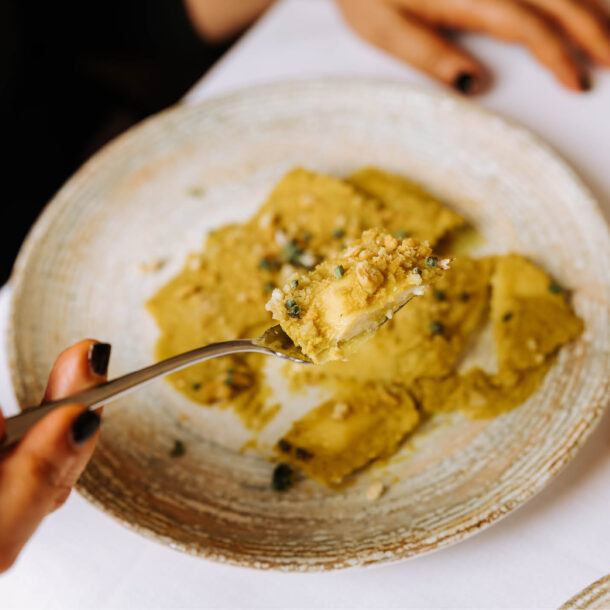 Ravioli con crema verde e granella, uno sollevato con la forchetta