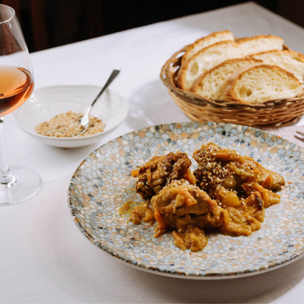 Carne in umido con carote e granella su un piatto a mosaico, con pane e un calice di rosato