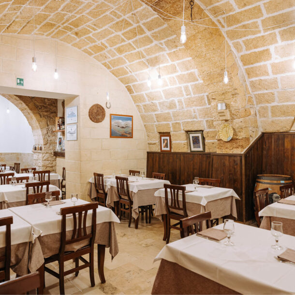Sala con volta in pietra, tavoli apparecchiati e vetrina di bottiglie